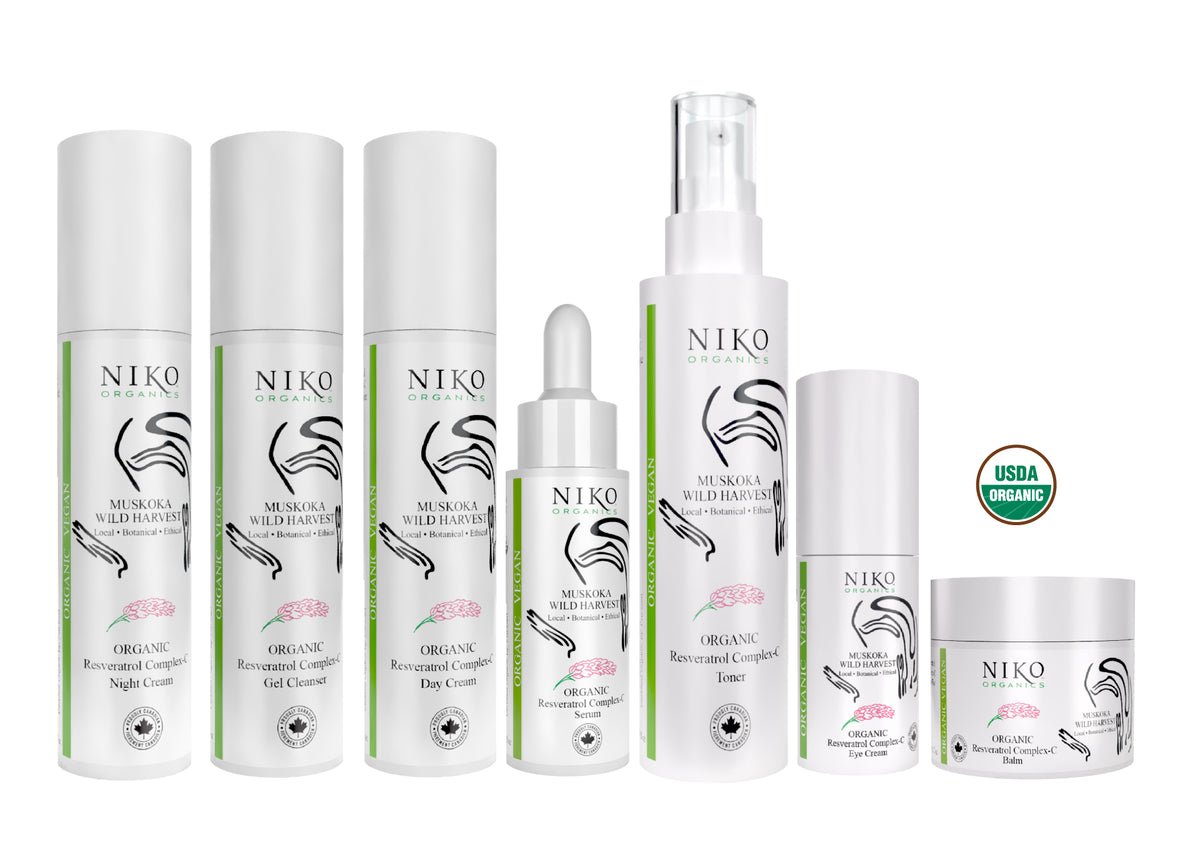 A set of white NIKO skin care products on a white background, including bottles, a dropper bottle, a pump bottle, and a jar, with a green USDA Organic seal.